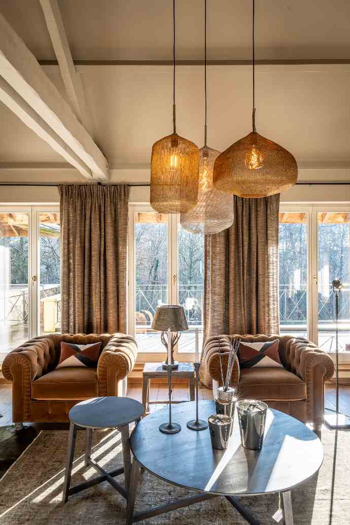 Intérieur salon avec fauteuils en daim luxueux, table ronde, tapis et lumière naturelle.