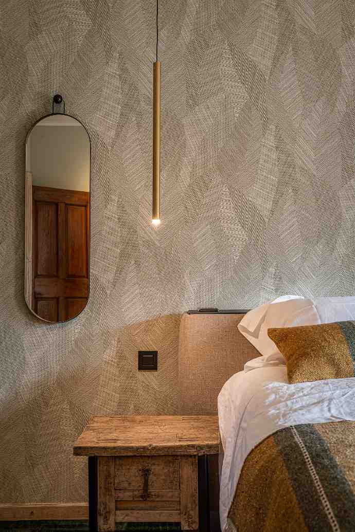 Chambre élégante avec mur à motifs géométriques, miroir ovale, suspension fine et table de nuit rustique.