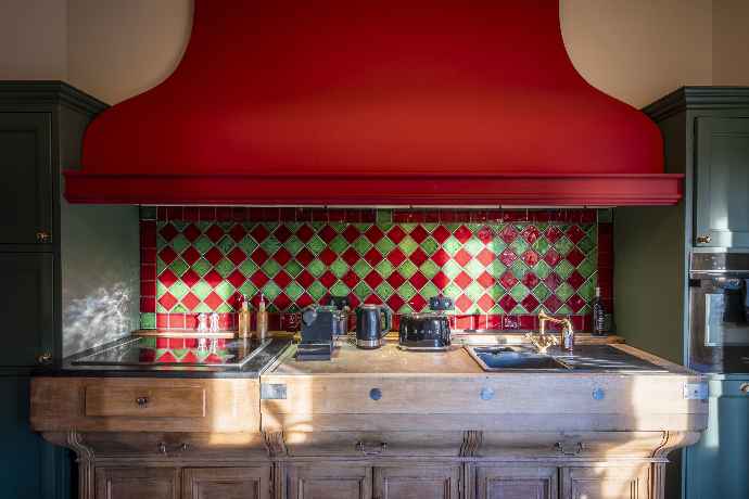 Cuisine rustique avec hotte rouge, carrelage vert et rouge, et meubles en bois ancien